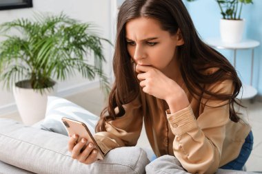 Evde cep telefonu mesajı okuyan endişeli genç bir kadın.