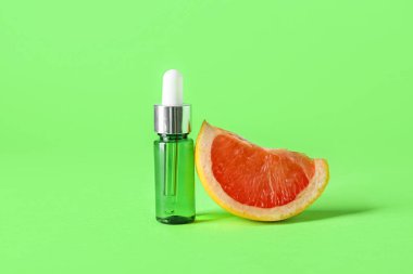 Yeşil arka planda bir şişe gerekli yağ ve greyfurt dilimi.