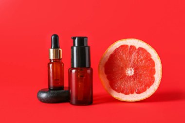 Önemli yağlı şişeler ve kırmızı arka planda yarım greyfurt.