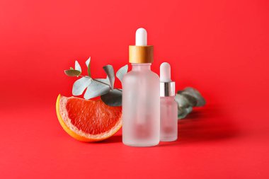 Kırmızı zemin üzerinde gerekli yağ şişeleri, bir parça greyfurt ve okaliptüs dalı