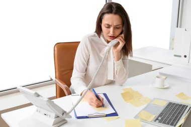 Genç yönetici iş yerinde telefonla konuşurken yapışkan kağıt üzerine yazıyor.