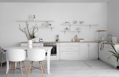 Yemek masası, mutfak tezgahı ve mutfak gereçleri olan şık bir mutfak.