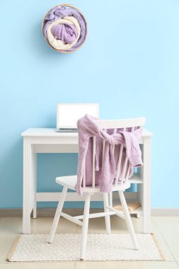 Mavi duvarın yanında dizüstü bilgisayarı ve örgü süveteri olan modern bir işyeri.