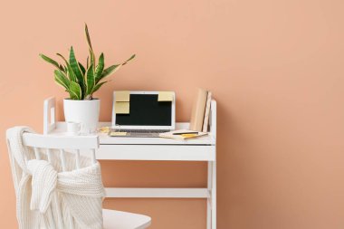 Dizüstü bilgisayarı, yapışkan notları, kahve fincanı ve bej duvarın yanındaki bitki örtüsü olan modern işyeri.