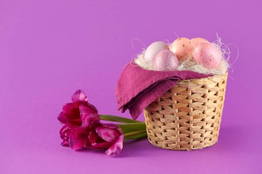Renkli arka planda boyanmış Paskalya yumurtaları ve çiçeklerle dolu bir sepet.