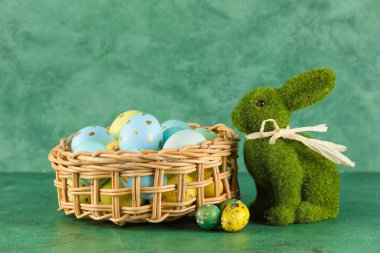 Yeşil arka planda boyanmış Paskalya yumurtaları ve oyuncak tavşancık sepeti.