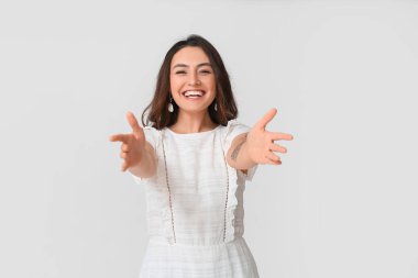 Gri arka planda sarılmak için kollarını açan mutlu genç kadın.