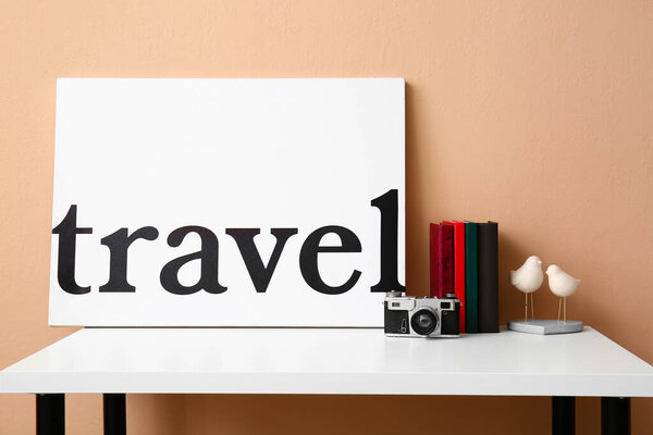 Books, stylish decor and poster with word TRAVEL on table near color wall