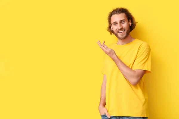 黄色の背景に何かを示すスタイリッシュなTシャツのハンサムな若い男 — ストック写真