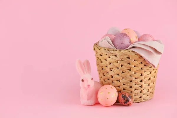 粉色背景的彩绘复活节彩蛋和玩具兔子柳条筐 — 图库照片