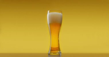 Sarı arka planda köpüklü bir bardak taze bira.
