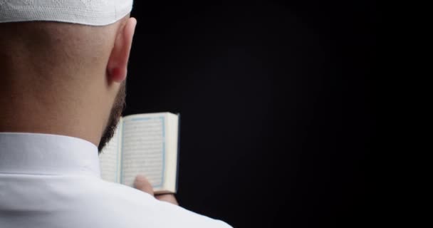 イスラム教徒の男性黒の背景にコーランを読んで バックビュー — ストック動画
