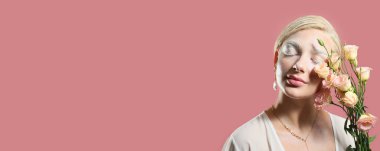 Yaratıcı makyajı ve pembe arka planda çiçekleri olan güzel genç bir kadın.