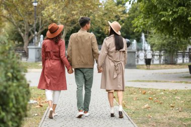 Man with two beautiful women walking in park. Polyamory concept clipart