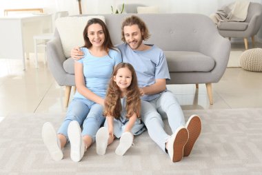 Genç bir aile evdeki yumuşak halıda oturuyor.