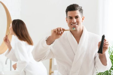 Genç bir çift banyoda aktif kömür diş macunu ile dişlerini fırçalıyor.