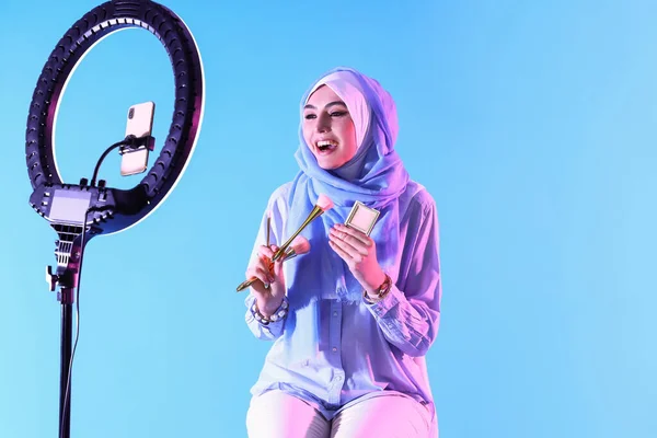 拥有化妆品刷和蓝色背景粉末录像的穆斯林美容博客 — 图库照片