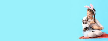 Tavşan kulaklı küçük kız ve açık mavi arka planda şirin Sphynx kedisi.