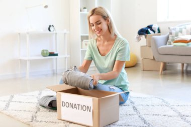 Genç bir kadın evde bağış yapmak için kıyafetlerini kutuya koyuyor.