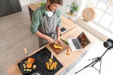 Genç adam mutfakta video dersi izlerken kabak kesiyor.