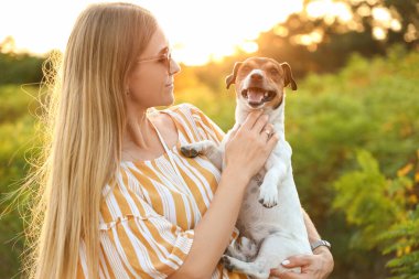 Genç bir kadın parkta sevimli Jack Russel köpeği tutuyor.