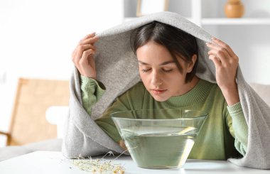 Genç bir kadın burun deliklerini rahatlatmak ve açmak için evde buhar solunumu yapıyor.