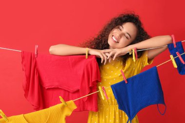 Kırmızı arka planda çamaşır asan ve mandalları olan genç bir Afro-Amerikalı kadın.