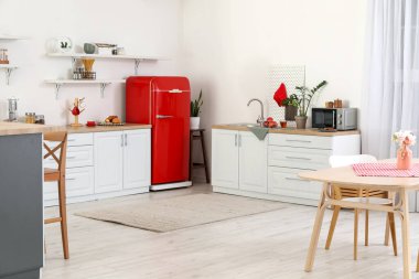 Kırmızı buzdolabı, tezgah ve raflı aydınlık mutfağın içi.