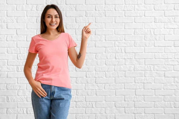 Junge Frau Leerem Shirt Zeigt Etwas Auf Weißem Backsteinhintergrund — Stockfoto