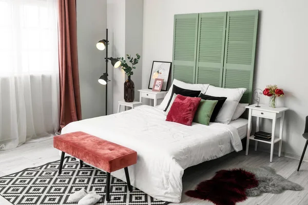 Interior of light bedroom with green folding screen and bench