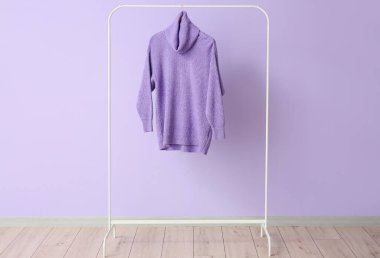 Renkli duvarın yanında leylak rengi süveter var.