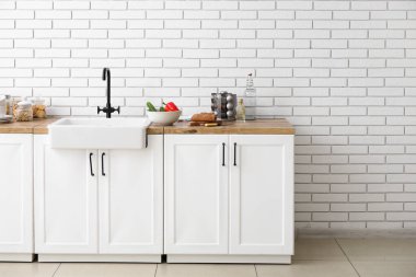 Lavabo, yemek ve mutfak gereçleri beyaz tuğla duvarın yanında.