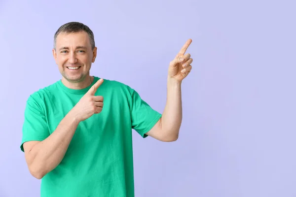 Reifer Mann Grünen Shirt Zeigt Auf Etwas Auf Fliederfarbenem Hintergrund — Stockfoto