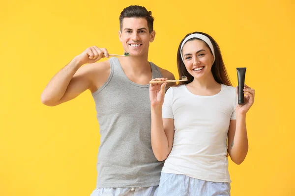Junges Paar Mit Aktivkohle Zahnpasta Und Bürsten Auf Gelbem Hintergrund — Stockfoto