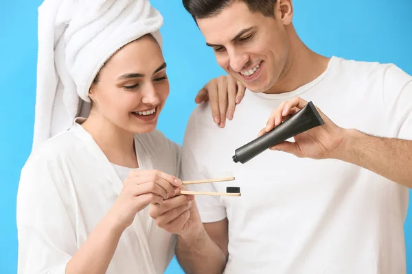 Junges Paar Mit Aktivkohle Zahnpasta Und Bürsten Auf Blauem Hintergrund — Stockfoto