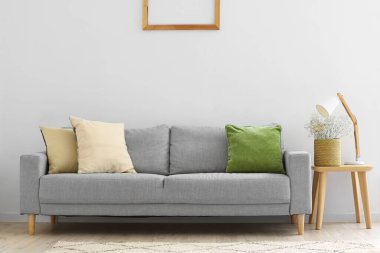 Gri kanepe, sepetinde çingene çiçekleri ve ışık duvarının yanında lamba olan masa.