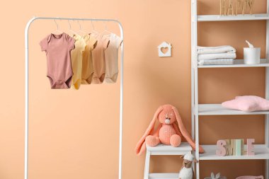 Süslü çocuk odasının içinde askılar, bebek kıyafetleri ve raf ünitesi var.