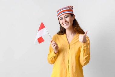 Endonezya bayrağı taşıyan genç Asyalı kadın ışık arka planında başparmak kaldırıyor