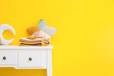 Sarı duvarın yanındaki masada oyuncak bebek kıyafetleri yığını.