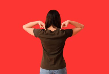 Kırmızı arka plandaki tişörte işaret eden genç bir kadın.