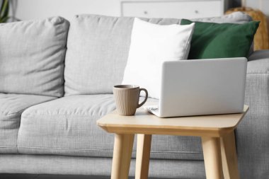 Hafif oturma odasında, bardaklı ve dizüstü bilgisayarlı tahta masa.