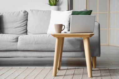 Hafif oturma odasında, bardaklı ve dizüstü bilgisayarlı tahta masa.