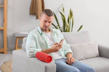 Cep telefonunu modern kablosuz hoparlöre bağlayan adam ışık odasındaki koltukta.