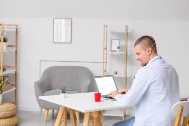 Adam dizüstü bilgisayarla çalışıyor ve masadaki kablosuz taşınabilir hoparlöre bakıyor.