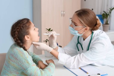 Doktor klinikte küçük kızın boğazını muayene ediyor.