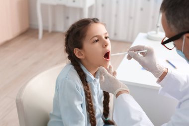 Doktor klinikte boğazı ağrıyan küçük bir kızı muayene ediyor.