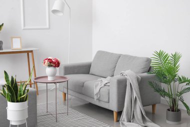 Masada şakayık çiçekleri, ev çiçekleri ve oturma odasında rahat koltuklar olan bir vazo.