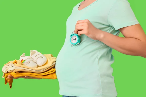 Kobieta Ciąży Stosem Ubrań Dla Niemowląt Budzikiem Zielonym Tle — Zdjęcie stockowe