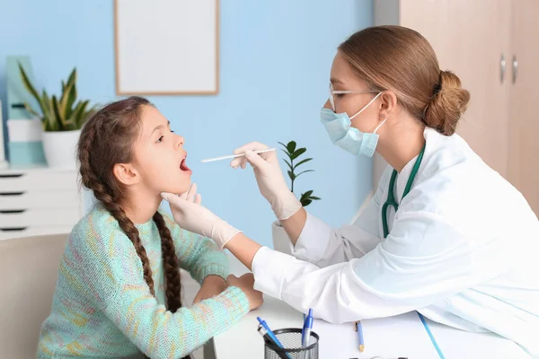 Doktor klinikte küçük kızın boğazını muayene ediyor.