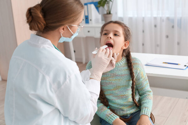 Doctor examining little girl with sore throat in clinic